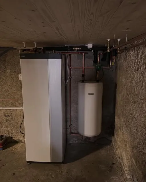 Installerad värmepump och varmvattenberedare med nya kopparrör i en källare