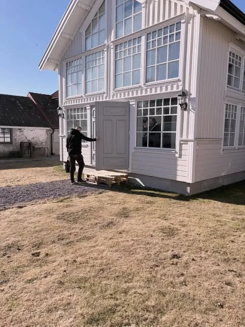 Montör vid entrén till ett vitt trähus en solig dag