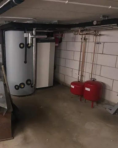 Teknikrum med ackumulatortank, värmepump, röda expansionskärl och kopparrör längs väggen